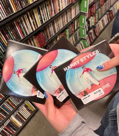 a person holding two dvd's in front of a book shelf filled with books