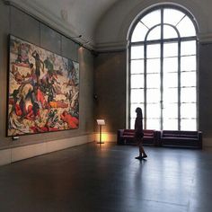 a woman standing in front of a large painting on the wall next to a lamp