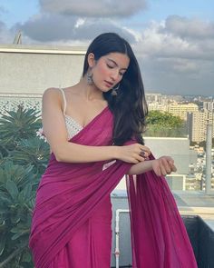 a woman in a pink sari posing for the camera on top of a building