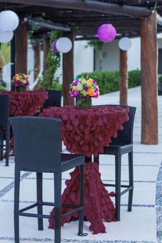 an outdoor dining area with black chairs and pink table cloths, lanterns and flowers