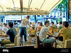 people sitting at tables in an outdoor restaurant eating food and talking to each other - stock image