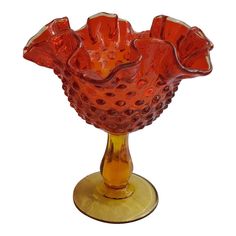 a red glass vase sitting on top of a gold plated stand with holes in it