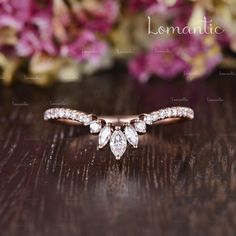 a close up of a diamond ring on a wooden table with flowers in the background