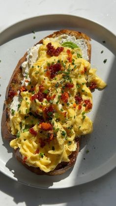 an open face sandwich topped with eggs and bacon on a white plate sitting on a table