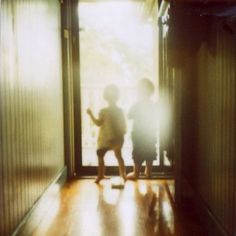 two children are standing in an open door with the light shining on them and one child is holding his hand out