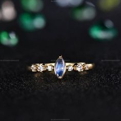 a gold ring with an oval shaped blue stone surrounded by smaller round diamonds on a black surface