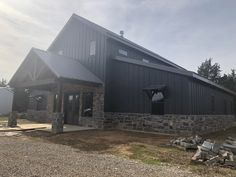 a large black barn sitting on the side of a road next to a pile of logs