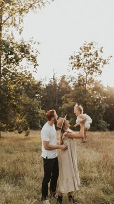 a family standing in a field holding their baby girl and looking at each other with trees in the background