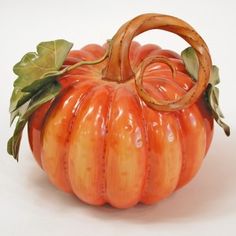 an orange ceramic pumpkin with green leaves on it's top and bottom, sitting in front of a white background