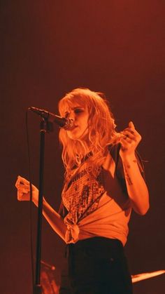 a woman standing in front of a microphone on top of a wooden stage with red lighting behind her