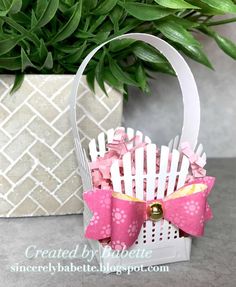 a white basket with pink bows sitting next to a potted plant