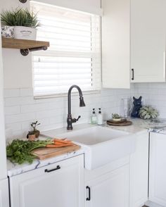 a kitchen with white cabinets and counter tops has plants on the window sill next to the sink