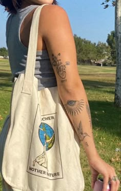 a woman with tattoos on her arm holding a white tote bag in the park