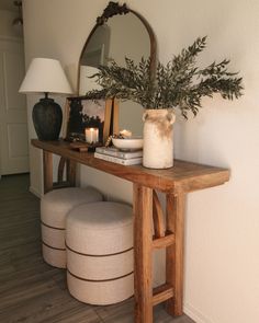 a wooden table topped with a vase filled with flowers next to a mirror and stool