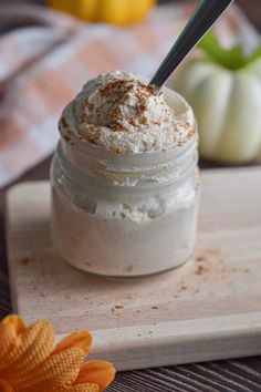 a small glass jar filled with whipped cream on top of a cutting board next to an orange flower