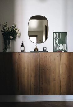 a wooden cabinet with a mirror and vase on top of it in front of a white wall