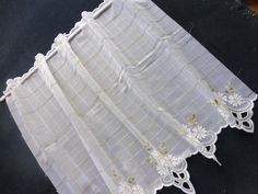 white curtains with yellow and white flowers are on a black tablecloth next to a pair of scissors