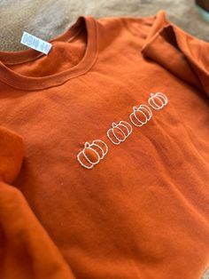 an orange shirt with pumpkins on it sitting on the floor next to a pair of scissors