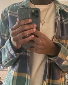 a person holding a cell phone in their hands and looking at the screen while wearing a flannel shirt