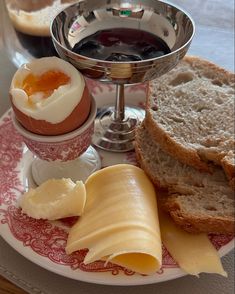 an assortment of cheeses, bread and jam on a red and white plate with a silver goblet