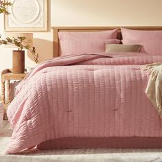 a bed with pink comforter and pillows in a bedroom