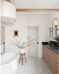 a bathroom with a large white tub and wooden cabinets in the corner, along with a vase filled with branches