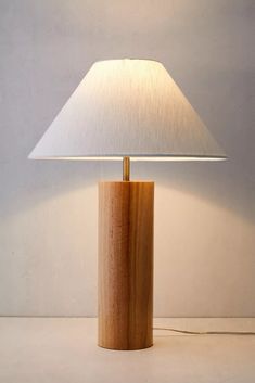 a wooden table lamp with a white shade on the base and a light that is turned on