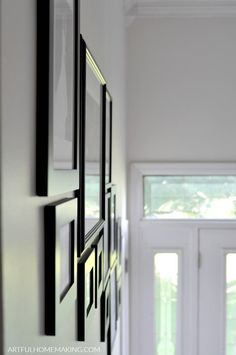 a hallway with white walls and black framed pictures on the wall, along with an open door leading to another room