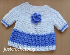 a blue and white crocheted sweater with a flower on the front, sitting on a wooden surface