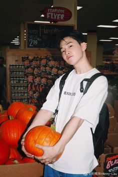 a young man holding a pumpkin in front of a pile of pumpkins at a grocery store