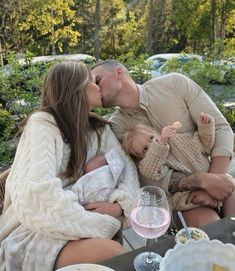 a man and woman kissing while holding a baby in front of a table full of food