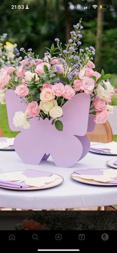 the table is set with pink and white flowers in purple vases, plates and napkins