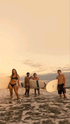 a group of people standing on top of a sandy beach holding surfboards in their hands