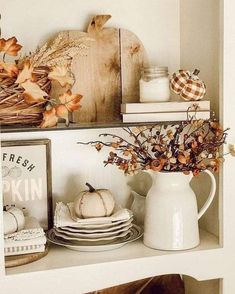 a shelf filled with plates and pumpkins on top of a wooden table next to a white pitcher