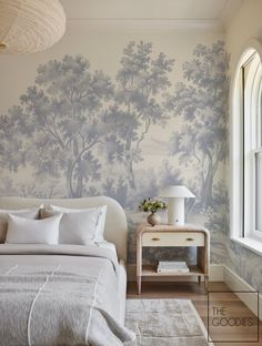 a bed sitting under a window next to a white table with a lamp on top of it