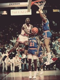 two basketball players jumping up to dunk the ball in front of an audience at a game