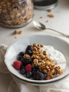 a bowl filled with granola and berries on top of a white table cloth next to a jar of yogurt