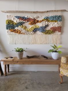 a wall hanging made with yarn and plants on a wooden table next to a yellow chair