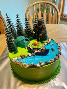 a birthday cake with a fishing scene on the top and trees in the middle, sitting on a table next to a chair