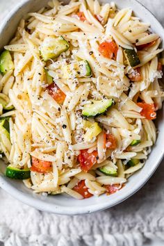 a bowl filled with pasta and vegetables on top of a white cloth next to a fork