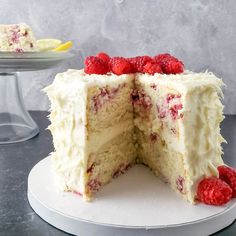 a cake with white frosting and raspberries is cut in half on a plate