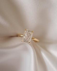 a diamond ring sitting on top of a white satin material with the center stone in yellow gold