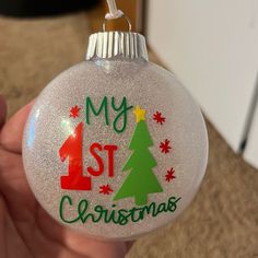 a hand holding a glass ornament with a christmas tree on it that says my 1st christmas