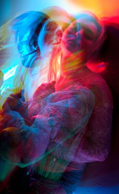 two women standing next to each other in front of a colorful light painting on the wall