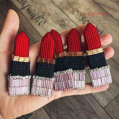 four red, black and white beaded lipsticks are held in a person's hand