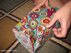 a person is opening a colorful gift box on the floor in front of a carpet