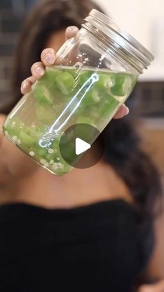 a woman holding a mason jar filled with pickles and cucumber in it