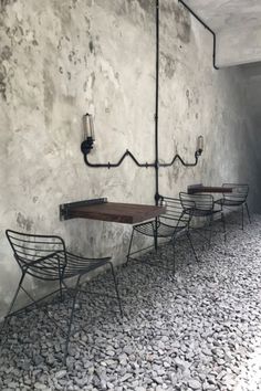 three metal chairs sitting next to each other in front of a wall with rocks on it