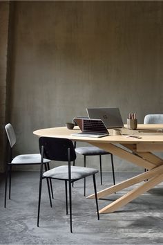 a wooden table with two laptops on top of it and chairs around the table