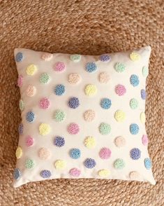 a white pillow with multicolored dots on it sitting on top of a couch